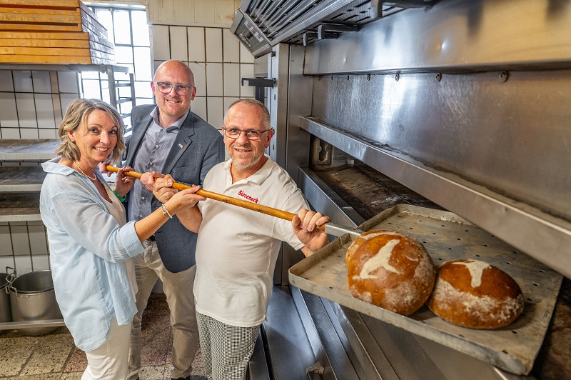 Zoodirektorin Astrid Stewin, Oberbürgermeister Sören Link und Bäckermeister Josef Sieveneck stehen vor dem Ofen. Auf einem großen Schieber liegen Brotlaibe. Ein aus Mehl aufgetragener Seelöwe ziert das Brot